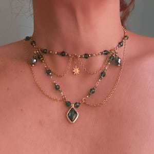 May include: A gold layered necklace with a green gemstone pendant and a star charm. The necklace is made of small beads and chains.