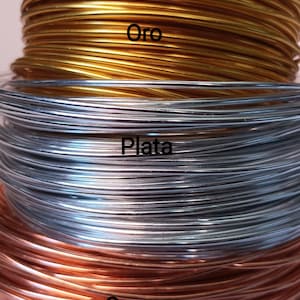 K&ouml;nnte beinhalten: Drei gestapelte Spulen aus d&uuml;nnem Metalldraht in den Farben Gold, Silber und Ros&eacute;gold. Die goldene Spule ist mit dem Text Oro beschriftet, die silberne Spule mit dem Text Plata und die ros&eacute;goldene Spule mit dem Text Oro rosa.