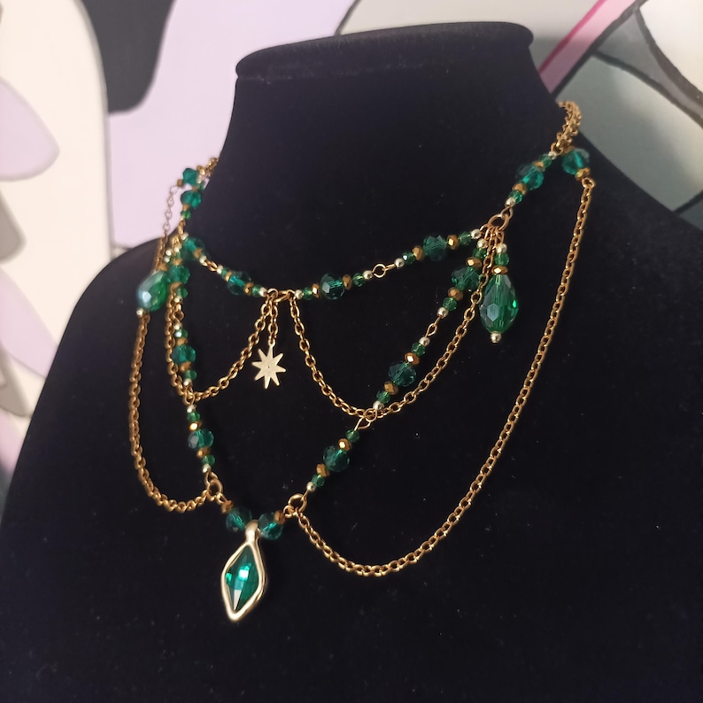 May include: A layered gold necklace with green crystal beads and a large green crystal pendant. The necklace has a star charm and a dangling green crystal drop.