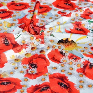 Puede incluir: Tela con estampado floral de amapolas rojas y margaritas blancas sobre un fondo claro. La tela está doblada, mostrando la impresión detallada de las flores.