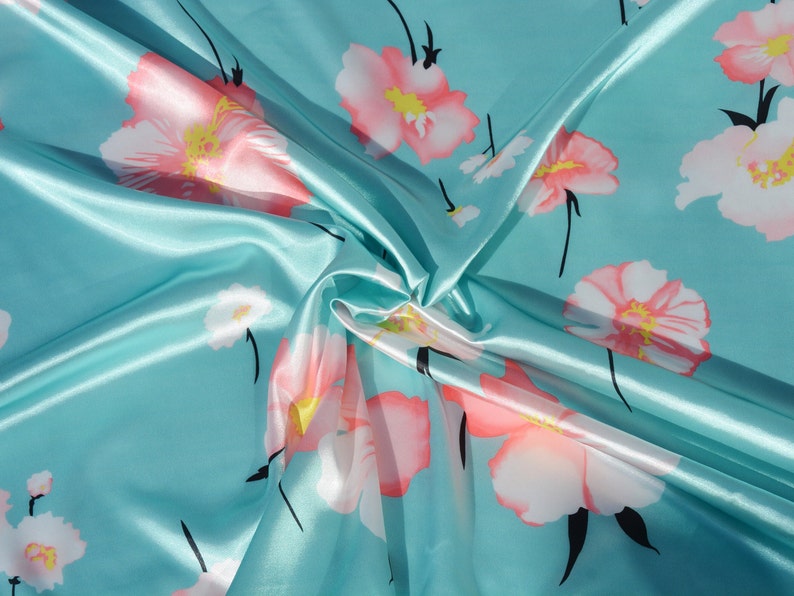 May include: A turquoise satin fabric with a floral print of pink and white flowers. The fabric is folded and draped, showing the texture of the satin.