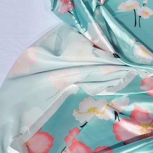 May include: A turquoise blue fabric with a floral print of pink and white flowers. The fabric is silky and has a sheen.