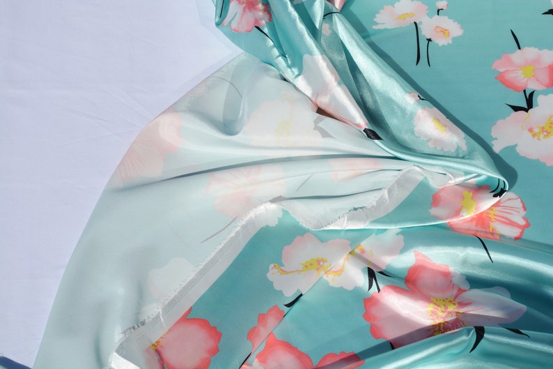 May include: A turquoise blue fabric with a floral print of pink and white flowers. The fabric is silky and has a sheen.