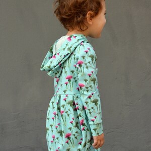 Puede incluir: Vestido con capucha azul claro con un estampado floral en rosa y verde. El vestido tiene mangas largas y una falda plisada. La capucha est&aacute; forrada con tela blanca. El vestido est&aacute; dise&ntilde;ado para ni&ntilde;os.