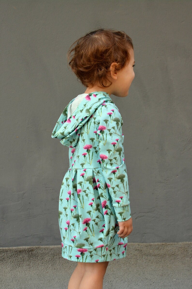 Puede incluir: Vestido con capucha azul claro con un estampado floral en rosa y verde. El vestido tiene mangas largas y una falda plisada. La capucha est&aacute; forrada con tela blanca. El vestido est&aacute; dise&ntilde;ado para ni&ntilde;os.