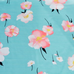 May include: A turquoise fabric with a repeating pattern of pink and white flowers. The flowers have a yellow center and black stems.