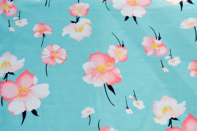 May include: A turquoise fabric with a repeating pattern of pink and white flowers. The flowers have a yellow center and black stems.