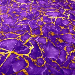 May include: Purple fabric with a gold marble pattern. The fabric has a smooth, silky texture.