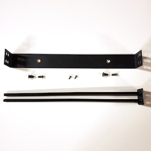 May include: Black metal hardware kit, including a long, rectangular bracket with angled ends and pre-drilled holes, two parallel rods, and several screws. The components are arranged on a white surface.