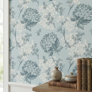 May include: A pale blue floral wallpaper with large hydrangea blooms in blue and white. The wallpaper is on a wall next to a wooden table with books and small ceramic vases.
