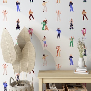 Pode incluir: Uma parede branca adornada com ilustrações coloridas de pessoas em trajes inspirados nos anos 70. As figuras estão em várias poses, sugerindo dança ou movimento. Uma cesta de vime com folhas grandes e texturizadas e uma mesa de madeira com objetos decorativos estão em primeiro plano.