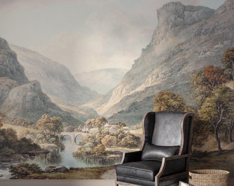 May include: A watercolor painting of a mountain valley with a river, bridge, and small village. The painting is framed and hanging on a wall in a room with a black leather armchair and a wicker basket.