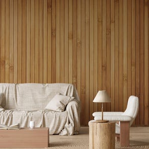 Może przedstawiać: Biała sofa z narzutą i poduszkami stoi przed drewnianą ścianą. Biały fotel z lampą stoi obok drewnianego stołka. Na podłodze leży tkany dywan.