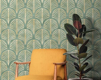 May include: A mustard yellow armchair with wooden arms and legs sits in front of a wall covered in teal and gold patterned wallpaper. A potted plant with dark green leaves is to the right of the chair.