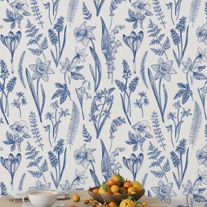 May include: A white background with a blue floral pattern. The pattern includes various flowers, leaves, and ferns. A wooden table with a bowl of oranges sits in the foreground.