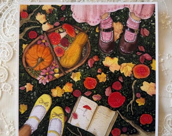 May include: A square art print featuring an illustration of a person in a pink skirt and brown shoes standing near a basket filled with a pumpkin, squash, and red mushrooms. An open book with a mushroom drawing lies on the ground among autumn leaves.