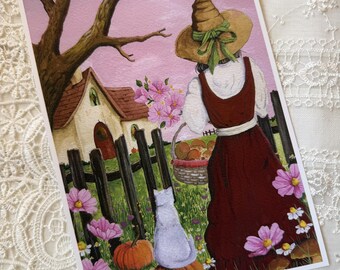 May include: A rectangular art print featuring a person in a brown dress and a pointed hat standing near a cottage. A white cat sits on a pumpkin in the foreground. The scene includes a dark wooden fence, pink flowers, green grass, and a bare tree.