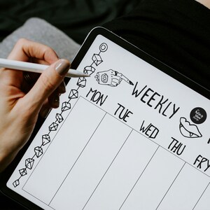 May include: A white weekly planner with black ink. The planner has a column for each day of the week, Monday through Friday. There are small illustrations of a hand with a pointing finger, a mouth with fangs, and a circle with the text "Graphic Novel Design".