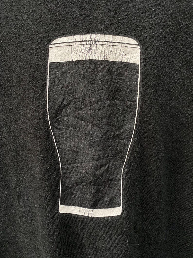 May include: Black sweatshirt featuring a graphic of a pint glass filled with a dark liquid. The pint glass design is outlined in white, with a white band at the top. The sweatshirt is made of a soft, textured fabric.