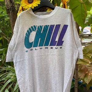 May include: A gray t-shirt with a blue, green, and purple "CHILL" graphic with the word "COLUMBUS" underneath.