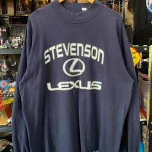 May include: Navy blue long-sleeve sweatshirt with the text "STEVENSON" above the Lexus logo and the word "LEXUS" below. The sweatshirt has a crew neck and is hanging on a wooden hanger.