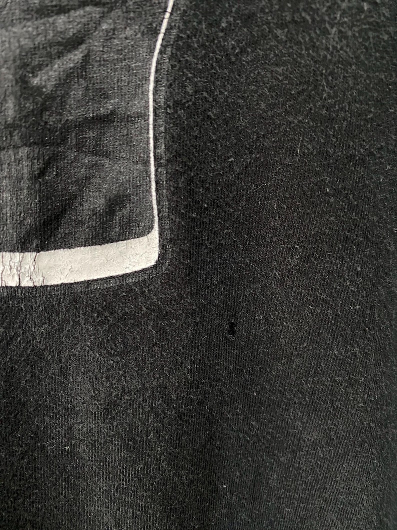May include: Close-up of a black garment with a rectangular patch and a white trim. The fabric has a textured appearance. The patch is a darker shade of black and has a reflective quality.
