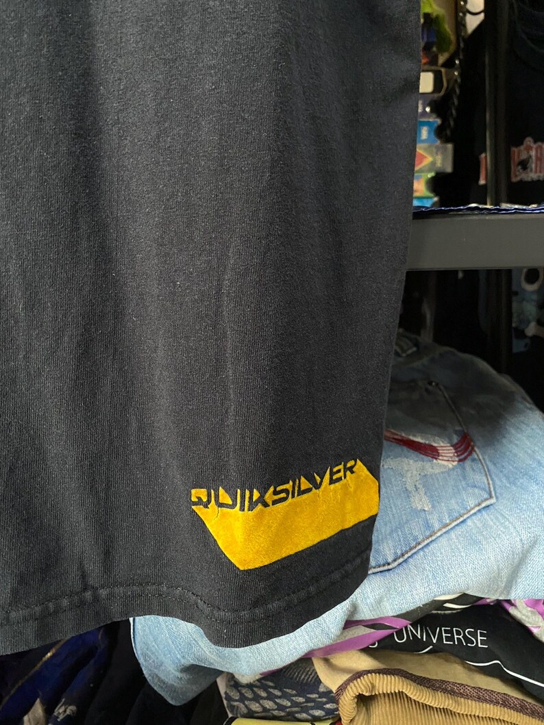 Pu&ograve; includere: Maglietta nera con logo "QUIKSILVER" giallo in basso a destra.