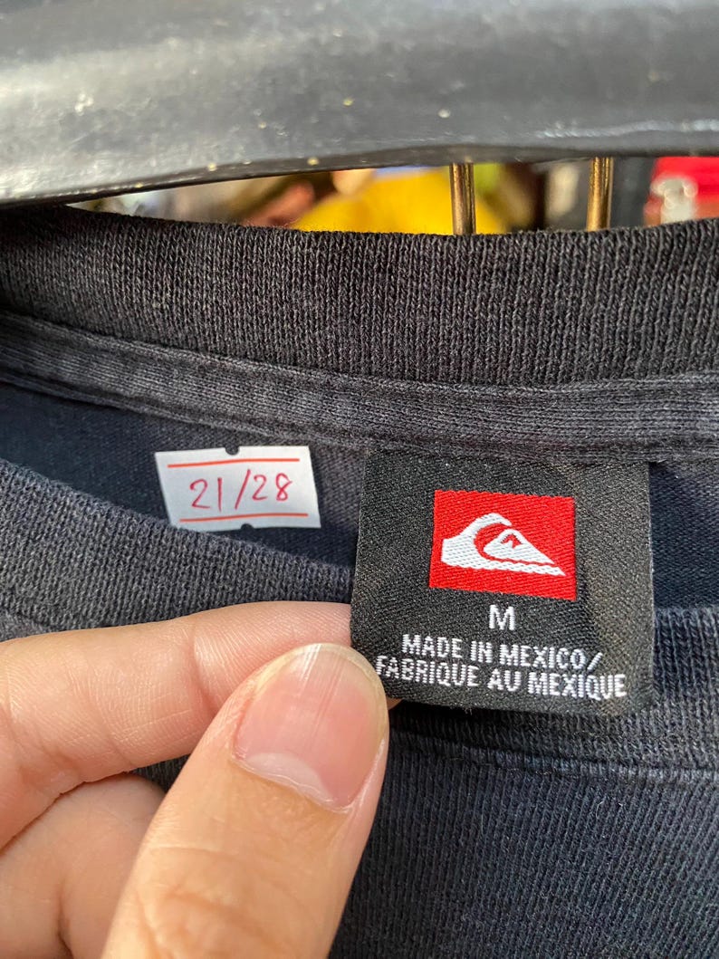 Pu&ograve; includere: Maglietta nera con un'etichetta bianca che dice "21/28" e un'etichetta nera con un logo rosso e il testo "M MADE IN MEXICO/FABRIQUE AU MEXIQUE"