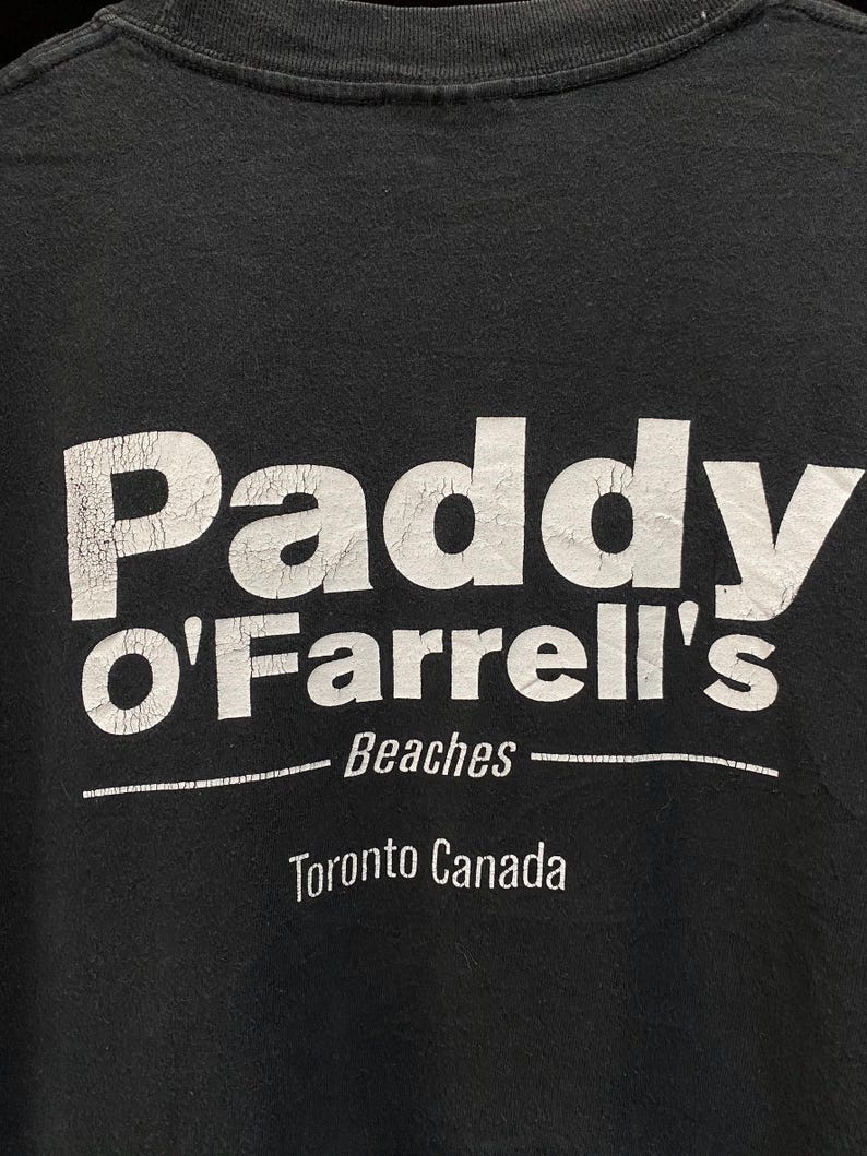 May include: Black t-shirt with the white text "Paddy O'Farrell's Beaches Toronto Canada". The text has a distressed, vintage look. The shirt is a casual wear item.