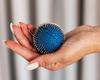 May include: A blue spiky massage ball with silver metal spikes. The ball is being held in a person's hand.