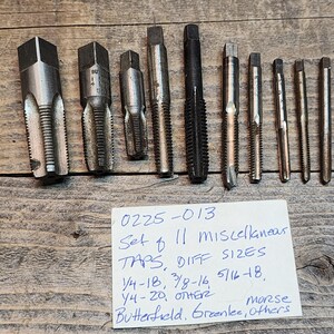 May include: A set of 11 assorted metal taps in various sizes. The taps are labeled with the text "0225-013 Set of 11 Miscellaneous Taps, Diff Sizes 1/4-18, 3/8-16, 5/16-18, 1/4-20, Other Morse Butterfield, Greenlee, Others".