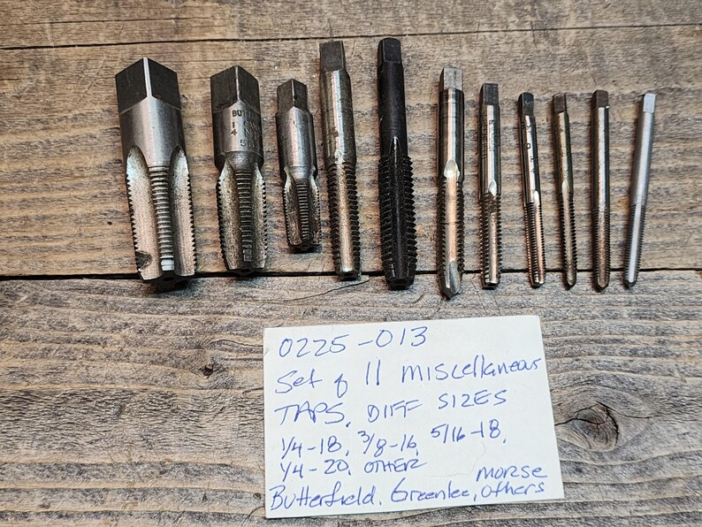 May include: A set of 11 assorted metal taps in various sizes. The taps are labeled with the text "0225-013 Set of 11 Miscellaneous Taps, Diff Sizes 1/4-18, 3/8-16, 5/16-18, 1/4-20, Other Morse Butterfield, Greenlee, Others".