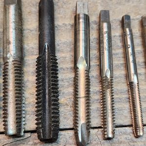 May include: A set of eight metal tap and die sets with different sizes and thread counts. The tap and die sets are silver and black in color.