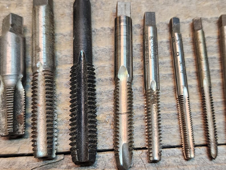 May include: A set of eight metal tap and die sets with different sizes and thread counts. The tap and die sets are silver and black in color.