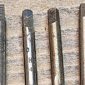 May include: Four silver metal tap and die sets with different sizes and markings. The sets are on a wooden surface.