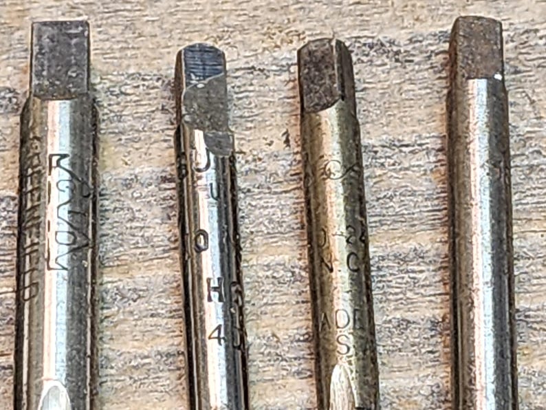 May include: Four silver metal tap and die sets with different sizes and markings. The sets are on a wooden surface.