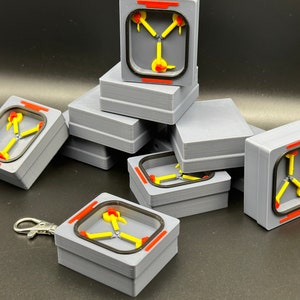 May include: A set of eight grey boxes with a yellow and red design inside. The boxes are stacked on top of each other. The design inside the boxes is a stylised representation of a flux capacitor.