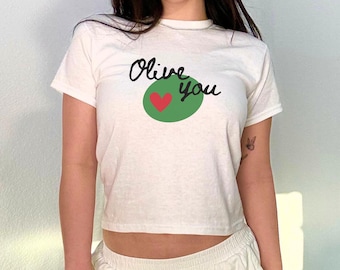 May include: A white cropped t-shirt with the text "Olive you" and a green olive with a red heart inside. The person is wearing white pants and a silver handbag.