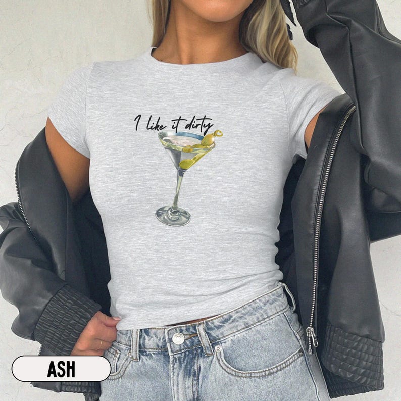 May include: A gray t-shirt with the text "I like it dirty" and a martini glass with olives. The shirt is being worn by a person with a black leather jacket.
