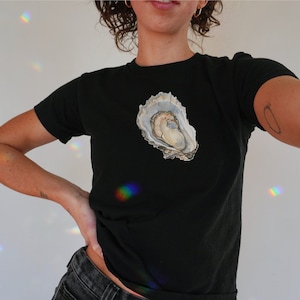 May include: A black t-shirt featuring a white oyster shell graphic on the front.