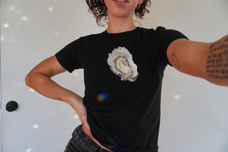 May include: A black t-shirt featuring a white oyster shell graphic on the front.