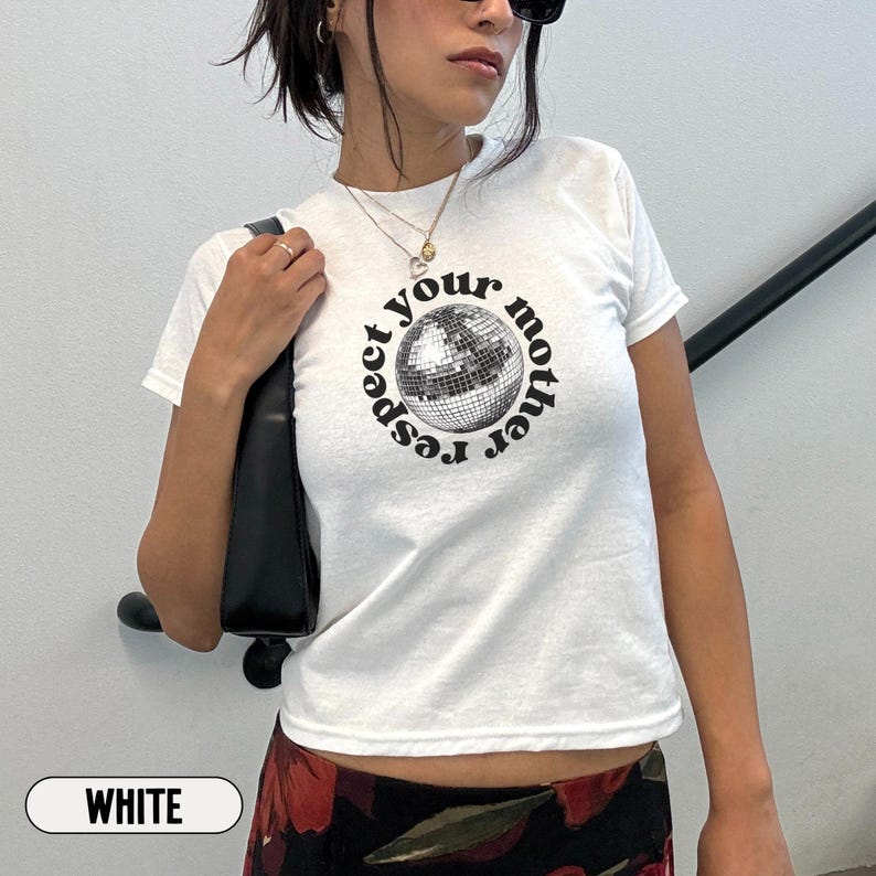 Puede incluir: Una camiseta blanca de manga corta con un gr&aacute;fico de una bola de discoteca plateada centrado en el pecho. El texto "respect your mother" est&aacute; impreso en una fuente negra circular alrededor de la bola. La camiseta tiene cuello redondo y corte entallado.