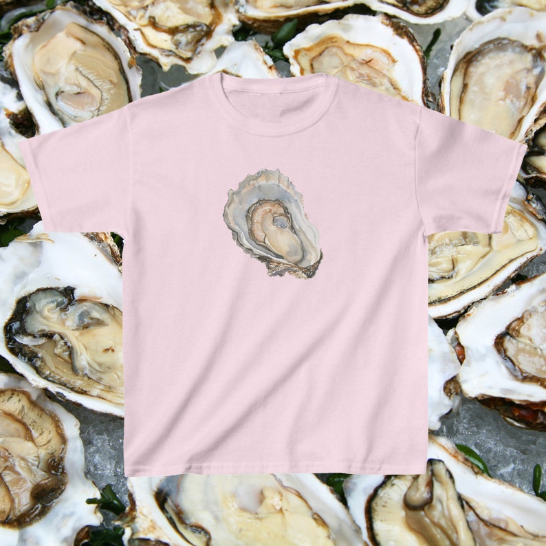 May include: A pink t-shirt featuring a single oyster printed on the front. The oyster is open and the inside is visible.
