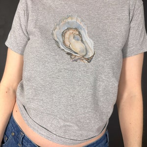 May include: A grey t-shirt with a watercolour illustration of an oyster shell on the front.