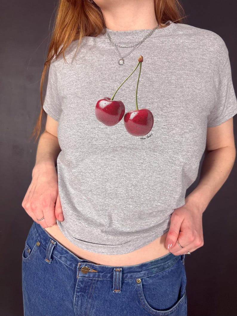 May include: A gray t-shirt with a graphic of two red cherries on the front. The cherries have stems and leaves.