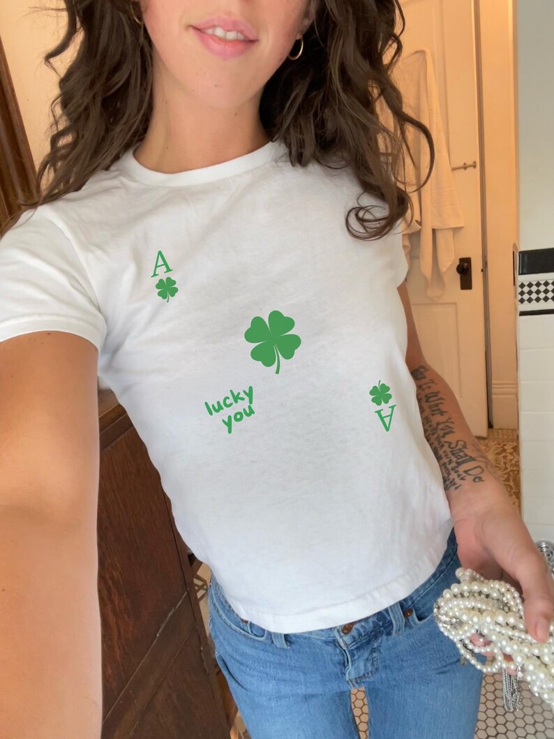 May include: White t-shirt with a green four-leaf clover and the text "lucky you" printed on it.