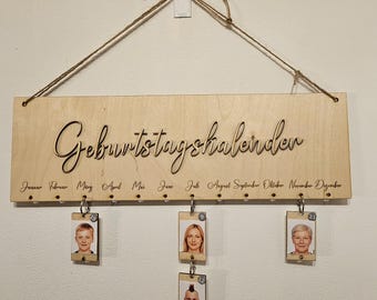 May include: Wooden birthday calendar with the German text "Geburtstagskalender" and months listed below. Includes small photo tags hanging below the calendar. The calendar is suspended by a twine string.