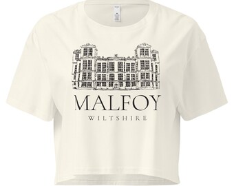 Może przedstawiać: Kremowy top z czarno-białą ilustracją architektoniczną. Tekst "MALFOY WILTSHIRE" jest wydrukowany poniżej w kroju szeryfowym. Koszulka ma krótkie rękawy i okrągły dekolt.