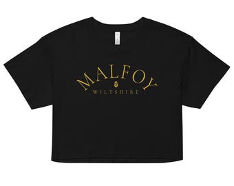 Może przedstawiać: Czarny crop top ze złotym napisem "MALFOY", wygiętym nad napisem "Wiltshire". Koszulka ma krótkie rękawy i okrągły dekolt. Tekst jest wyśrodkowany na przodzie koszulki.