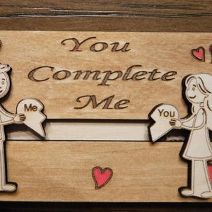 Può includere: Targa in legno con incisa la scritta "You Complete Me". Raffigura un uomo e una donna che tengono in mano pezzi di puzzle. Il design include cuori rossi. Un'idea regalo romantica. Misure in centimetri.
